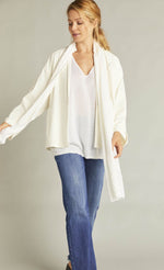 Load image into Gallery viewer, Front full body view of a woman wearing blue jeans and the white indies voyageur jacket. This jacket is open and layered over a white top with a with scarf. The jacket has a single front button, long sleeves, and a flared fit.
