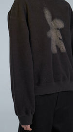 Load image into Gallery viewer, Front close up view of the front of a woman wearing the jnby rabbit sweater. This sweatshirt is smoke/black colored with a light grey rabbit on the front.
