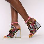 Load image into Gallery viewer, Outer and inner side view of a woman wearing the calypso kicker heel sandals from kat maconie. These open toe sandals have a tall framed heel, an ankle strap and embroidered, multicolored birds of paradise flowers covering the  sides of the foot.
