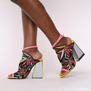 Outer and inner side view of a woman wearing the calypso kicker heel sandals from kat maconie. These open toe sandals have a tall framed heel, an ankle strap and embroidered, multicolored birds of paradise flowers covering the  sides of the foot.