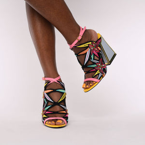 Front view of a woman wearing the calypso kicker heel sandals from kat maconie. These open toe sandals have a tall framed heel, an ankle strap and embroidered, multicolored birds of paradise flowers covering the  sides of the foot.