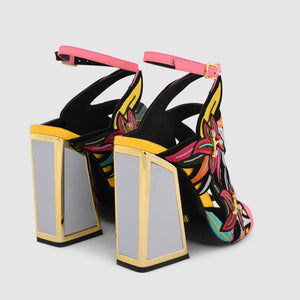 back side view of a pair of the calypso kicker heel sandals from kat maconie. These open toe sandals have a tall framed heel, an ankle strap and embroidered, multicolored birds of paradise flowers covering the  sides of the foot.