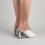 Load image into Gallery viewer, Outer side view of a woman wearing a pair of the kat maconie fai mule. This show has an open back and an open toe with a layered over blush/white upper. The white heel is geometric and outlined with black.
