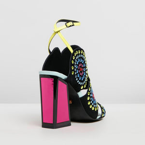 Back, Outer side view of the kat maconie frida multibrights high heels. This shoe is black with multicolored rhinestones arranged in circles. The toe and back are open. The shoe features a yellow ankle strap and a pink high heel with a black outline.