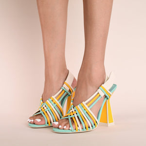 Front inner and outer side views of a model wearing a pair of the kat maconie sheri sandal. This strappy sandal has a high heel and a mix of turquoise, yellow, and white colored straps. The white back strap is wider and adjustable. The heel is yellow and outlined with opal/white.
