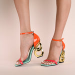 Load image into Gallery viewer, Outer and inner side view of a model wearing a pair of the kat maconie suzu high heel. This shoe has a blue/opal sole, an orange and pink patent leather upper with an adjustable ankle strap, and a gold chain-like heel.
