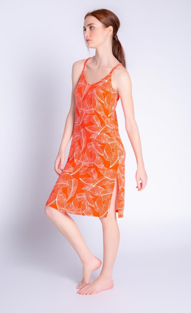 Front left side view of a woman wearing the pj salvage leafy dreams dress. This tank dress has a v-neck, long side slits, and is orange colored with a white tropical leaf print.