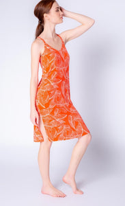 Front full body view of a woman wearing the pj salvage leafy dreams dress. This tank dress has a v-neck, long side slits, and is orange colored with a white tropical leaf print.