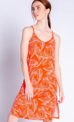 Load image into Gallery viewer, Front full body view of a woman wearing the pj salvage leafy dreams dress. This tank dress has a v-neck, long side slits, and is orange colored with a white tropical leaf print.
