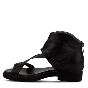 Inner side view of the l'artiste gladiator sandal in black. This sandal covers the heel and ankle with a black folded leather. The instep is covered with a strap that goes over it and another strap that goes over the toes.