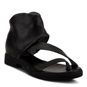 Outer side front view of the l'artiste gladiator sandal in black. This sandal covers the heel and ankle with a black folded leather. The instep is covered with a strap that goes over it and another strap that goes over the toes.