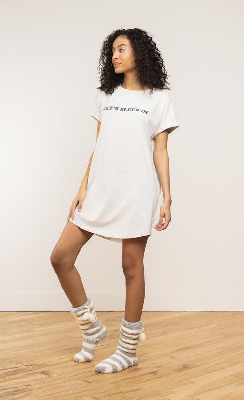 Front view of a woman wearing the coffee shoppe t-shirt dress. This t-shirt dress is grey with the words let's sleep in.