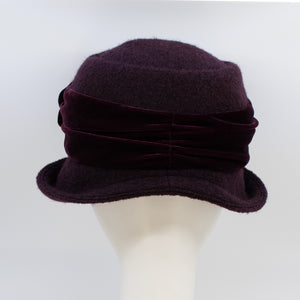 back view of the lillie & cohoe aubergine wool jeanette hat. This hat is wine/purple colored and has a rounded brim and a velvet band that wraps around the crown to make a bow on the side.