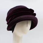 Load image into Gallery viewer, left side view of the lillie &amp; cohoe aubergine wool jeanette hat. This hat is wine/purple colored and has a rounded brim, ear warmers, and a velvet band that wraps around the crown to make a bow on the side.
