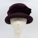 Load image into Gallery viewer, Front view of the lillie &amp; cohoe aubergine wool jeanette hat. This hat is wine/purple colored and has a rounded brim and a velvet band that wraps around the crown to make a bow on the side.
