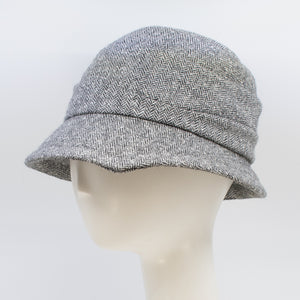 front left side of the lillie & cohoe herringbone vintage phoebe hat. This hat has an asymmetrical pointed brim, a layered crown, and a grey herringbone pattern.