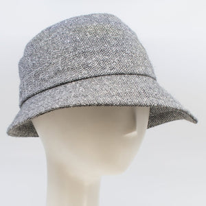 Front right side view of the lillie & cohoe herringbone vintage phoebe hat. This hat has an asymmetrical pointed brim, a layered crown, and a grey herringbone pattern.