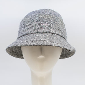 Front view of the lillie & cohoe herringbone vintage phoebe hat. This hat has an asymmetrical pointed brim, a layered crown, and a grey herringbone pattern.