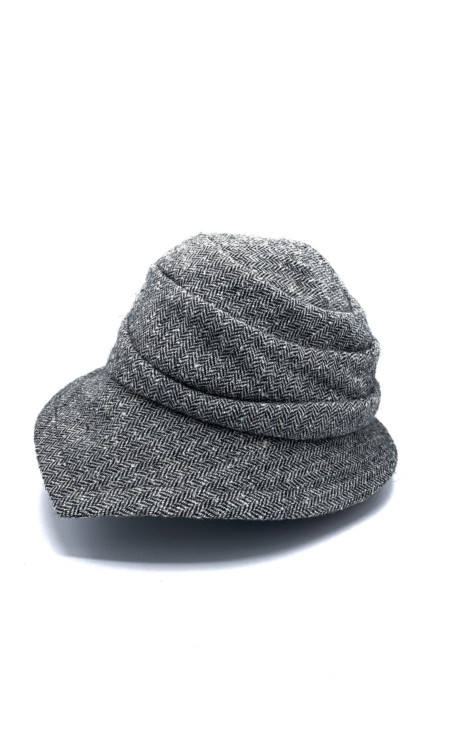 Left side view of the lillie & cohoe herringbone vintage phoebe hat. This hat has an asymmetrical pointed brim, a layered crown, and a grey herringbone pattern.