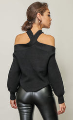 Load image into Gallery viewer, Back top half view of a woman wearing the Line &amp; Dot Cold Shoulder sweater tucked into black leather pants. This black sweater has a criss cross neck that exposes the shoulder and long sleeves.
