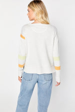 Load image into Gallery viewer, Back, top half view of a woman wearing jeans and the Lisa Todd Aim High Sweater. The sweater is white with a yellow stripe and an orange stripe on both long sleeves, an extra orange stripe near the shoulder of the left arm, and a white back.

