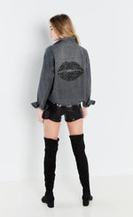 Load image into Gallery viewer, back full body view of a woman wearing the lisa todd black denim back talk shirt. This back of this shirt is decorated with stones that take the shape of lips. The shirt has long sleeves and a distressed hem.
