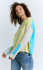 Load image into Gallery viewer, Front top half view of a woman wearing jeans and the lisa todd color crush sweater. This sweater is green/yellow in the front. It has drop shoulder long sleeves. The left sleeve is white while the right sleeve is pastel blue. The back of the sweater is sky blue.
