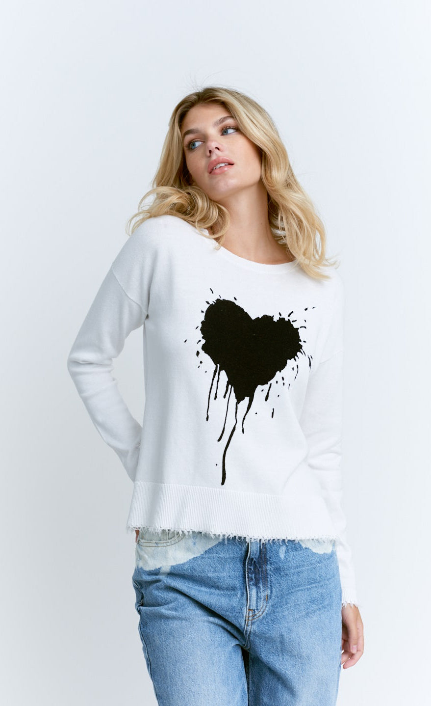 Front top half view of a woman wearing the lisa todd tainted love sweater. This sweater is white with a black dripping heart on the front.