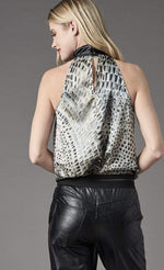 Load image into Gallery viewer, Back top half view of a woman wearing black pants and the lola &amp; sophie animal halter blouse. This halter top is sleeveless with a black faux leather collar and a keyhole back. The tank is white with a black animal print.
