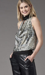 Load image into Gallery viewer, Front top half view of a woman wearing black pants and the lola &amp; sophie animal halter blouse. This halter top is sleeveless with a black faux leather collar and a draped cowl neck. The tank is white with a black animal print.
