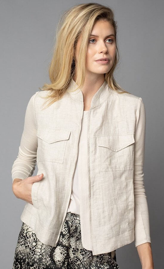 Front, top half view of a woman wearing the Lola & Sophie Crinkle Linen Jean Jacket. The sand colored jacket features two front, fold over breast pockets, a zipper front, a linen body, and fitted long sleeves.