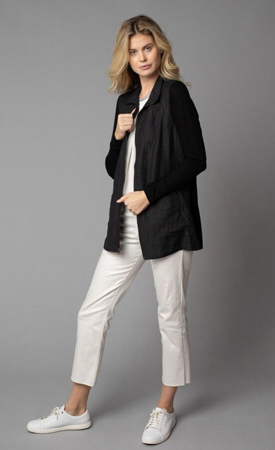 Front, left-sided full body view of a woman wearing white capris and the Lola & Sophie Crinkle Linen Zip-Front Long Black Jacket. This jacket has a flat collar, a zip up front, front pockets, and fitted long sleeves.
