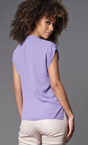 Back top half view of a woman wearing the lola & sophie Double Georgette Cap-Sleeve Top. this top is lavender colored, has side slits, and sits at the hips.