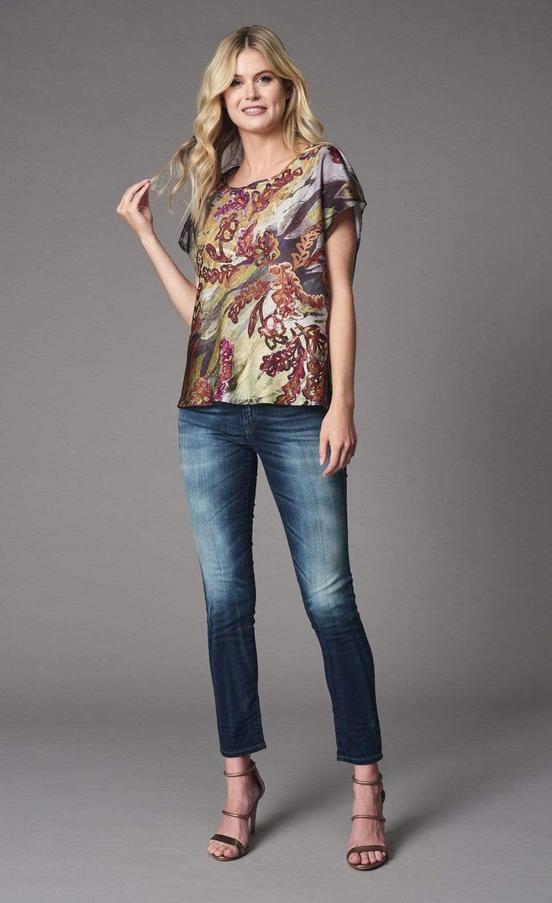 Front full body view of a woman wearing the lola & sophie fairytale top. This top has short sleeves and a bias cut. The print on the top has warm autumn colors mixed in with a wine colored floral print.