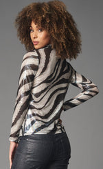 Load image into Gallery viewer, Back top half view of a woman wearing black pants and the lola &amp; Sophie foil zebra mesh turtleneck. This top has a white and silver zebra print all over it and long sleeves.
