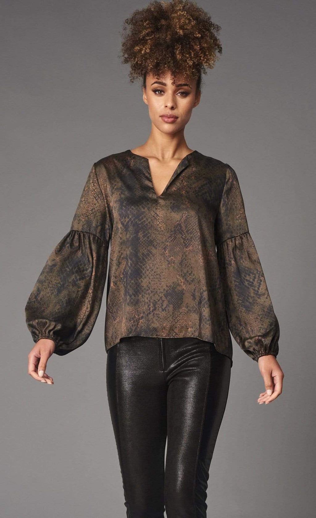 Front top half view of a woman wearing black leather pants and the lola & Sophie green python top. This top has a v-neck, balloon sleeves, and a brown/green washed python print on it.