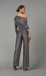 Load image into Gallery viewer, Back full body view of the lola &amp; sophie lurex jersey jumpsuit. This jumpsuit is silver colored with long sleeves, long wide pants, a tie belt at the waist, and a boat neck being worn off the shoulder.
