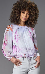 Load image into Gallery viewer, Front top half view of a woman wearing the lola &amp; sophie painted flower top. This top is white with a pink and red painted design sporadically on it. This top has long sleeves and a drawstring hem.
