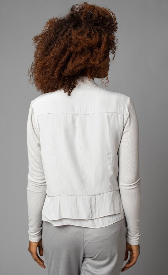 Back view of a woman wearing the no closure moto jacket from Lola & Sophie. This jacket is eggshell colored and thin with fitted sleeves and a tiered peplum bottom.