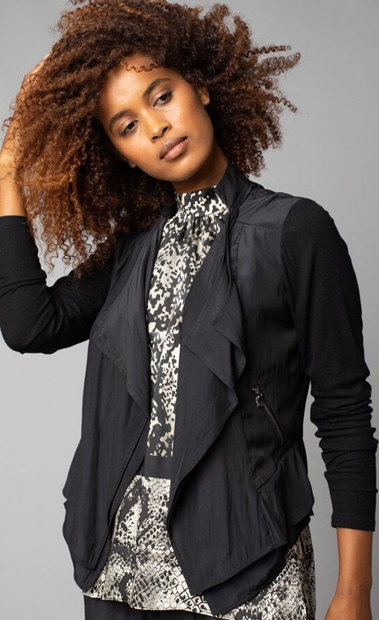 Front view of a woman wearing the no closure moto jacket from Lola & Sophie. The jacket in this picture is black and thin. It has fitted sleeves, a flowy satin front that drapes open, and front zipper pockets.