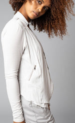 Load image into Gallery viewer, Side view of a woman wearing the no closure moto jacket from Lola &amp; Sophie. This jacket is eggshell colored and thin with fitted sleeves and a flowy satin front that has front zipper pockets.
