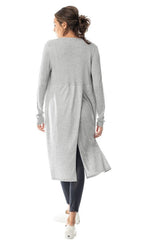 Load image into Gallery viewer, Back, full body view of a woman wearing the lola &amp; sophie split back cardi. This cardigan is grey and cuts off just below the model&#39;s knees. The long sleeves are fitted and ribbed. The back of this cardigan has an off-center right side slit running down the bottom half of it. On the bottom the woman is wearing skinny black pants.

