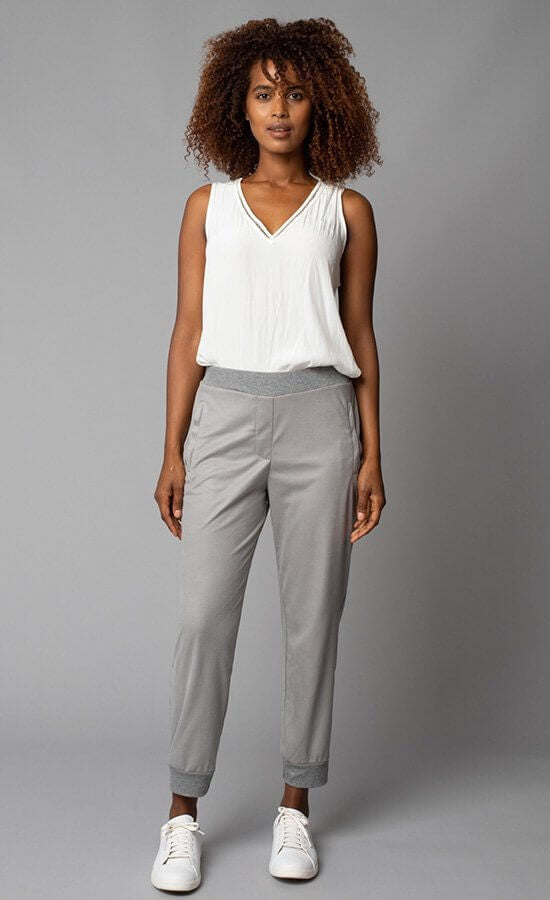 Front, full body view of a woman wearing the Lola & Sophie V-Neck tank tucked into grey ankle-length pants. This tank is eggshell colored and has detailed trim around the v-neck.