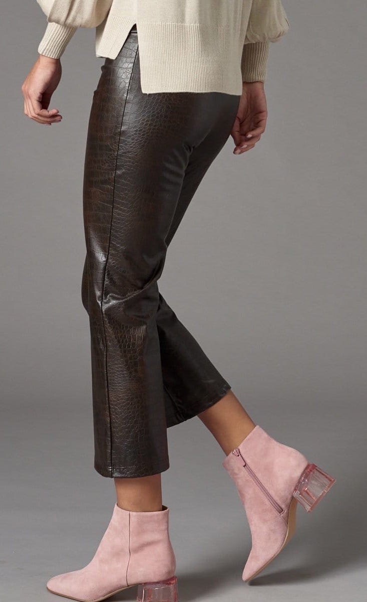 Left side bottom half view of a woman wearing the lola & sophie vegan leather kick flare pant. This pant is grey colored with a subtle crocodile print, a cropped leg, and a flared out bottom.