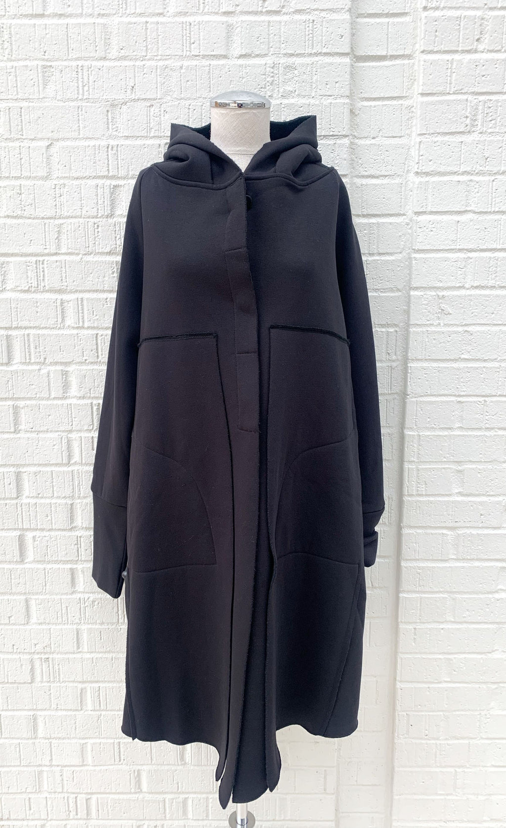 Front view of the black lotus eaters juniper coat on a mannequin. This coat has decorative stitching, long sleeves, and a closed front. The coat is knee length.