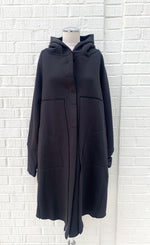 Load image into Gallery viewer, Front view of the black lotus eaters juniper coat on a mannequin. This coat has decorative stitching, long sleeves, and a closed front. The coat is knee length.
