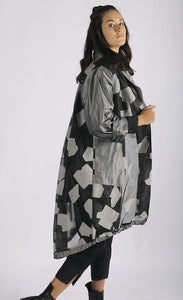 Right side full body view of a woman wearing the luukaa abstract jacquard organza jacket. This mid-length jacket has a black see-through organza body with grey sleeves, a grey collar, grey pockets, and a grey abstract print.
