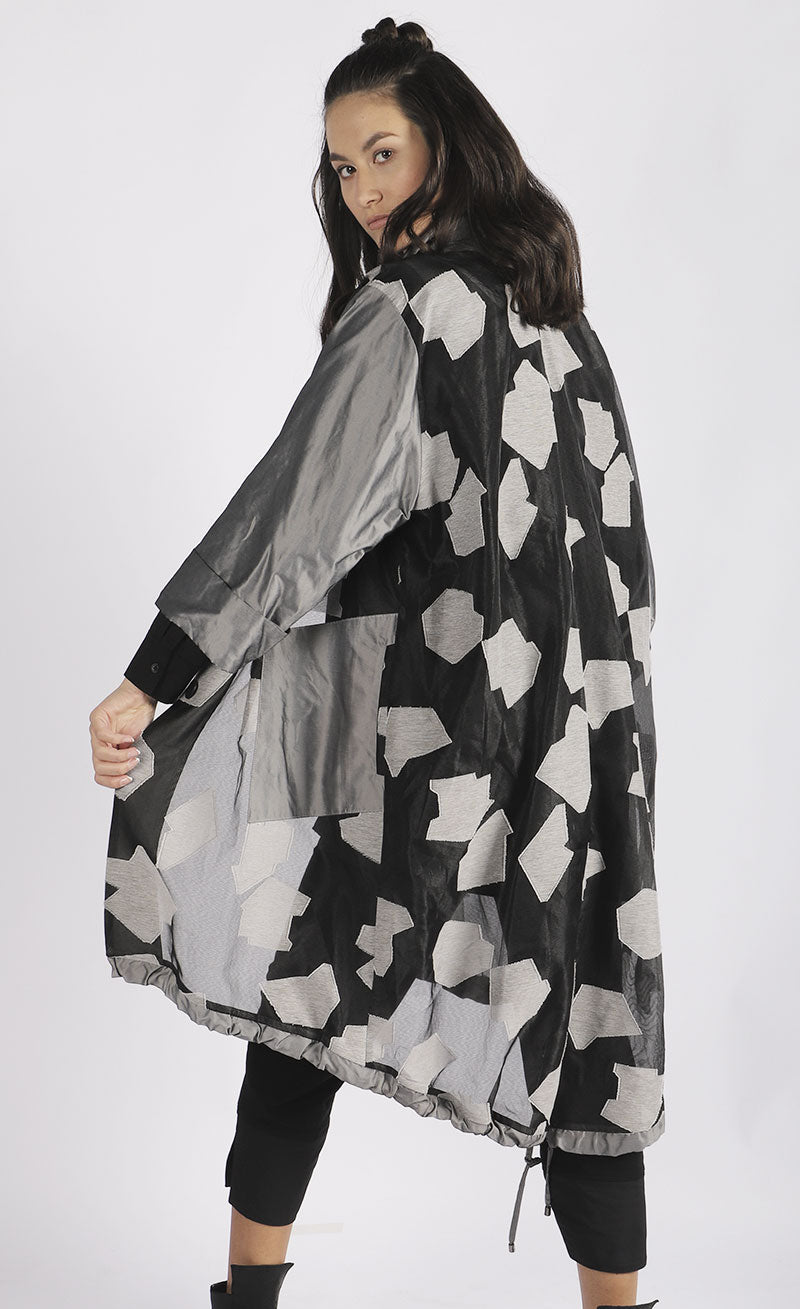Back full body view of a woman wearing the luukaa abstract jacquard organza jacket. This mid-length jacket has a black see-through organza body with grey sleeves, a grey collar, grey pockets, and a grey abstract print.
