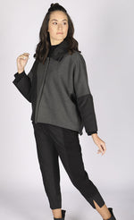 Load image into Gallery viewer, Front full body view of a woman wearing the luukaa short anthracite coat. This coat has a hidden front closure, and an anthracite body with black puffer fabric on the flat collar and long sleeves. The black puffer fabric also runs diagonally across the body
