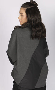 Back top half view of a woman wearing the luukaa short anthracite coat. This coat has an anthracite body with black puffer fabric on the flat collar and long sleeves. The black puffer fabric also runs diagonally across the body